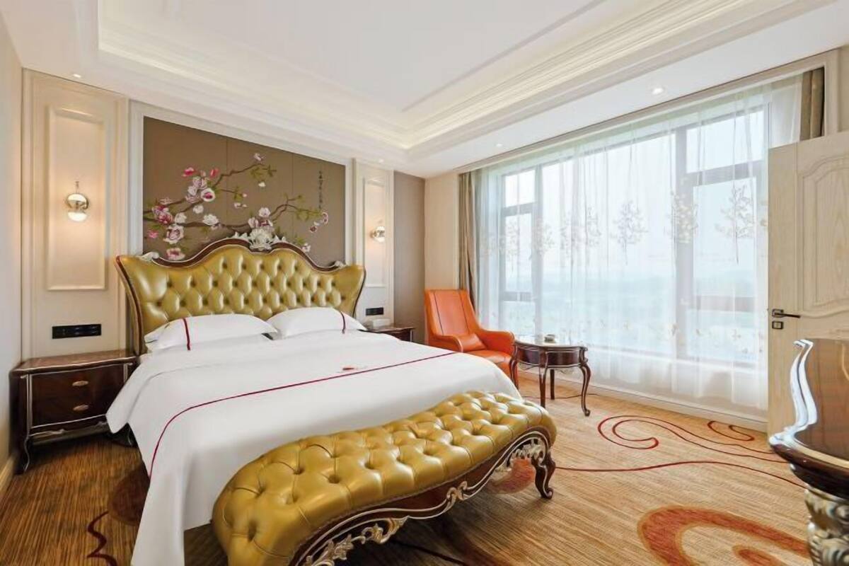 Une chambre d’hôtel avec un grand lit, une chaise, une petite table et une grande fenêtre.