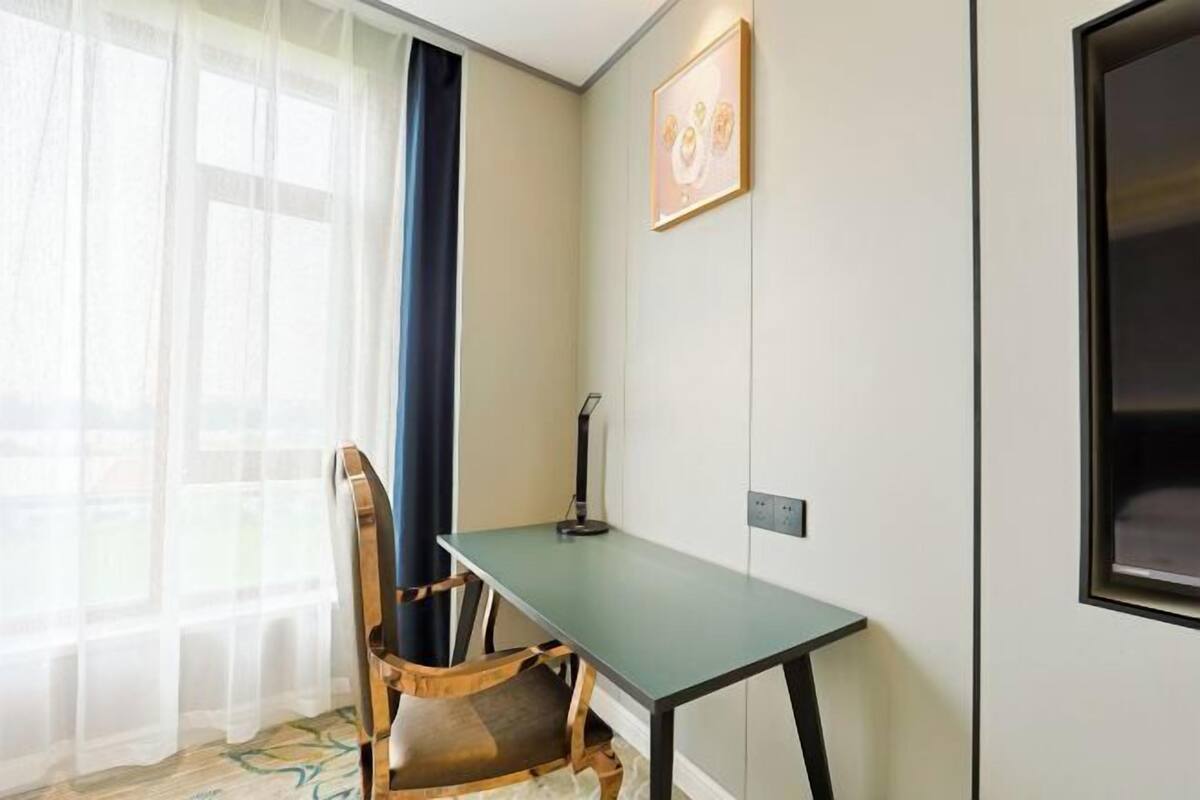 Une pièce comprenant un bureau, une chaise et une grande fenêtre ornée de rideaux légers.