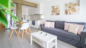 Ein modernes Wohnzimmer mit grauem Sofa, weißem Couchtisch und einem Essbereich mit weißen Stühlen.