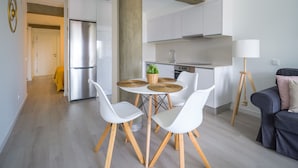 Eine moderne Küche mit weißen Schränken, einem Edelstahlkühlschrank und einem Essbereich mit weißen Stühlen und einem runden Tisch.