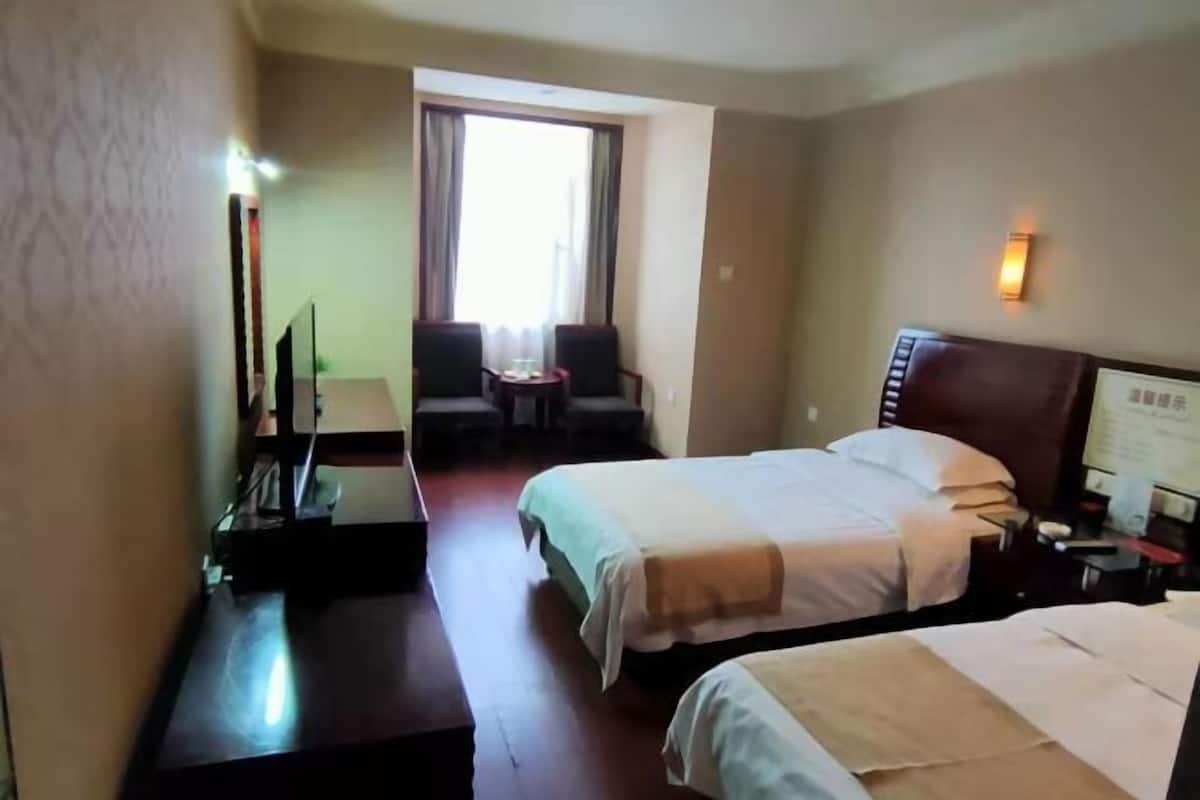 A hotel room with two beds, a desk, a chair, a TV, and a window with curtains.