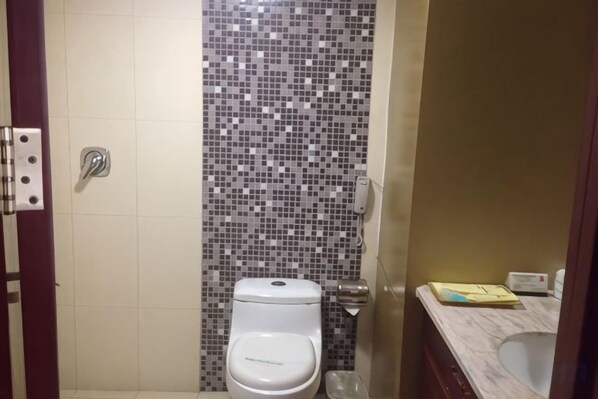 Un baño con pared de ducha azulejada, inodoro y lavamanos con espejo.