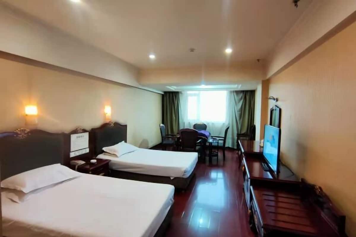 A hotel room with two beds, a desk, a chair, a TV, and a window with curtains.