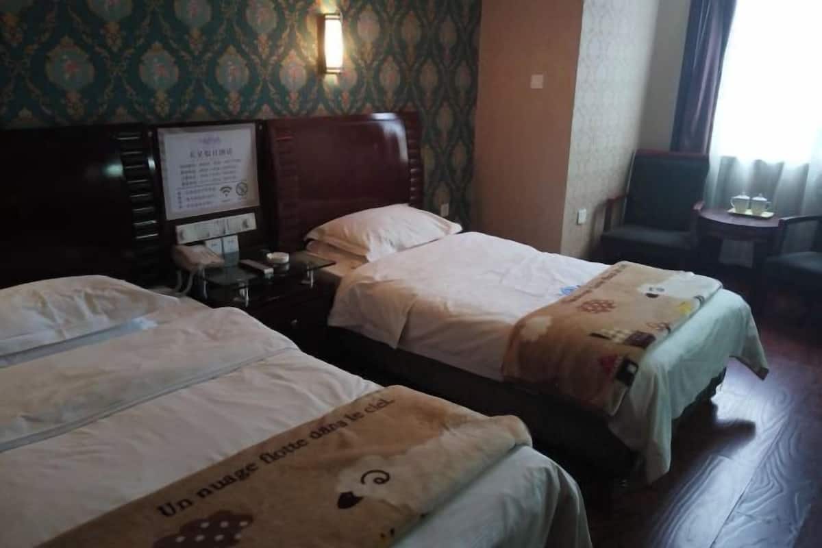 A hotel room with two beds, a nightstand, a lamp, a small table, and a chair.