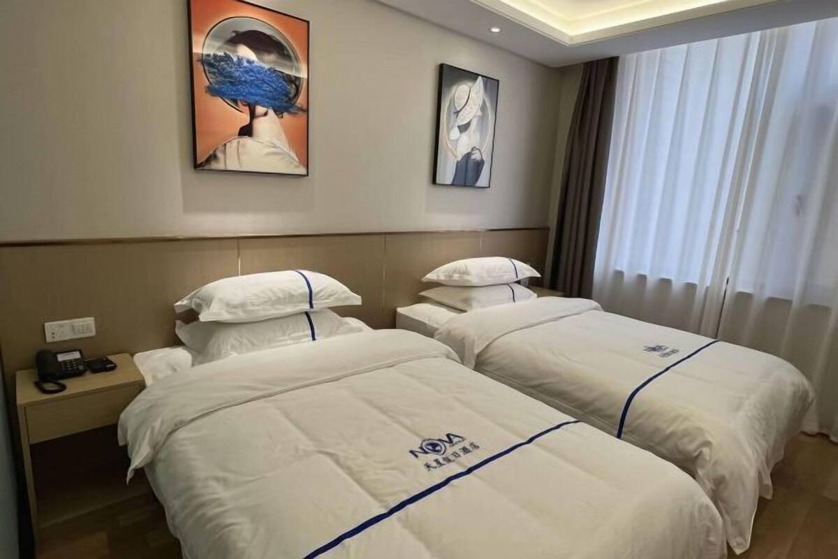 A hotel room with two beds, a nightstand with a phone, and artwork on the walls.