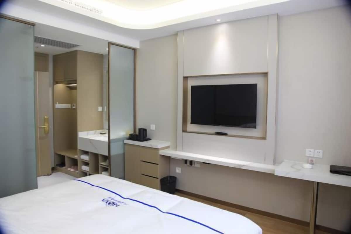 A modern hotel room with a bed, a TV mounted on the wall, a vanity with a mirror, and a small desk area.