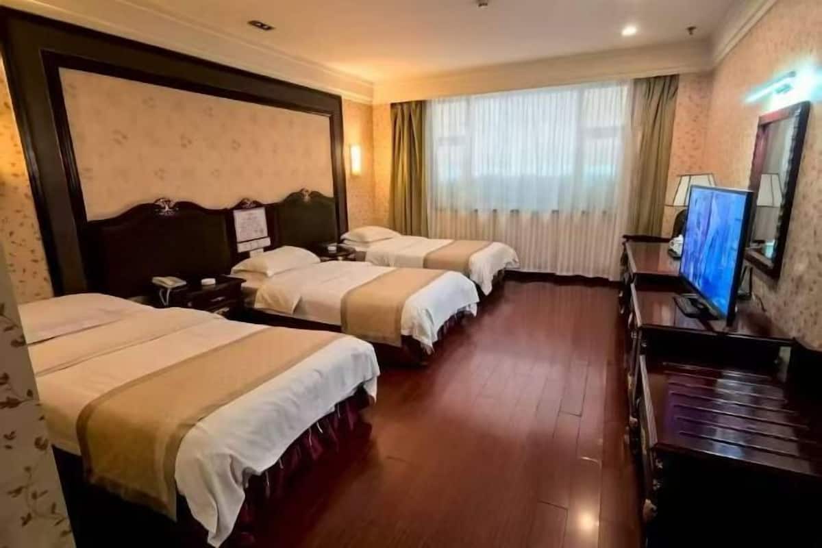A hotel room with three beds, a television, a desk, and a large window with curtains.