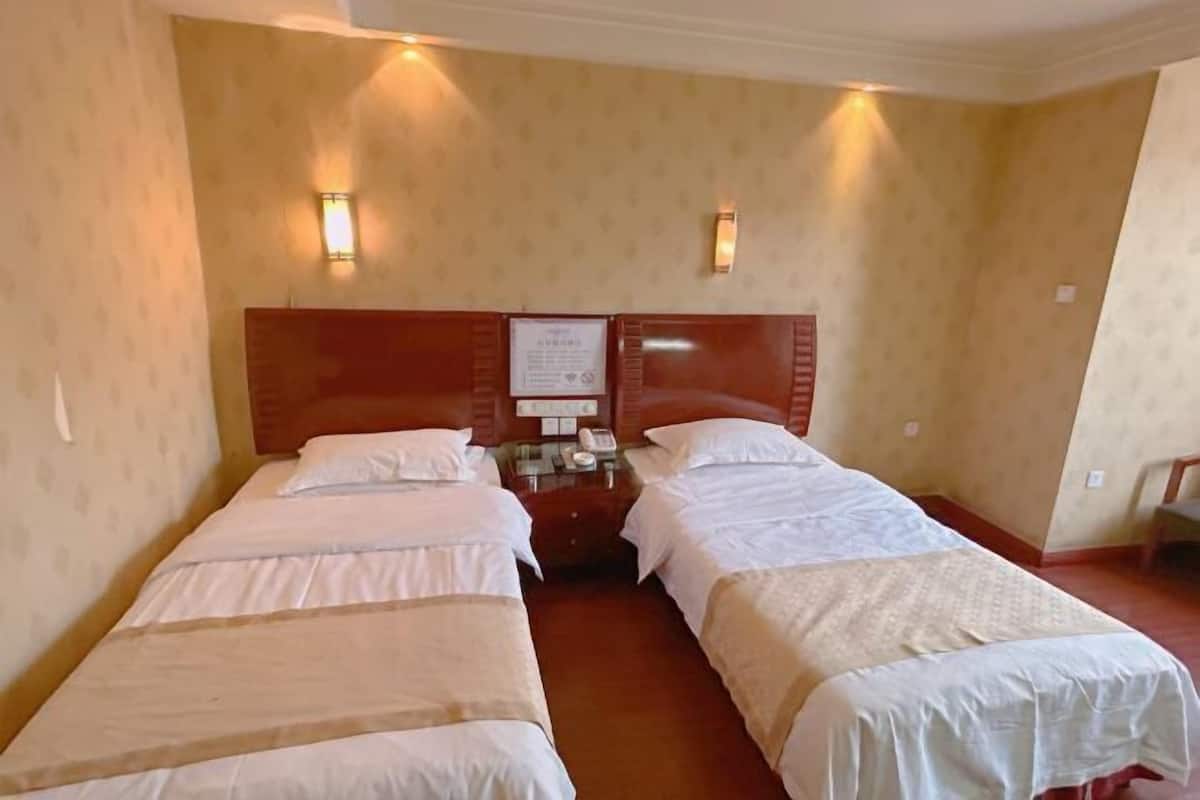 A hotel room with two single beds, a wooden headboard, a bedside table with a phone, and wall-mounted lights.