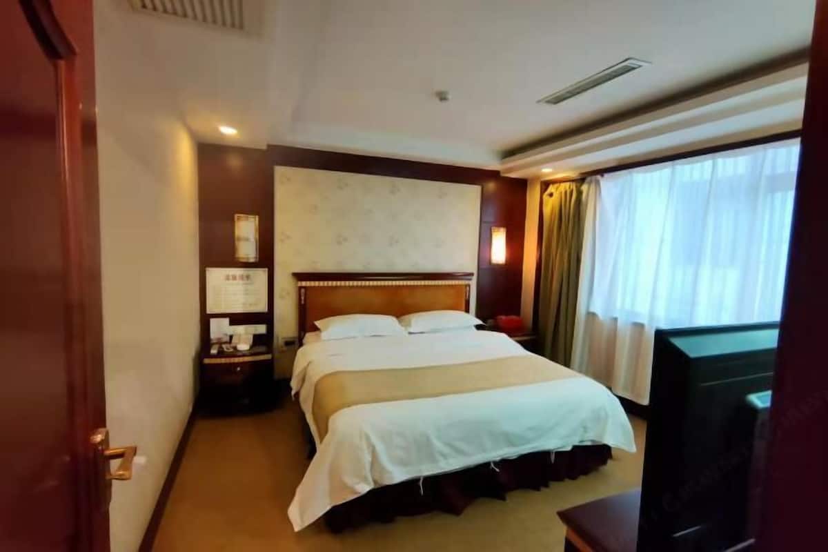 A hotel room with a large bed, a television, a nightstand, and a window with curtains.