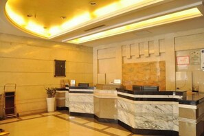 A hotel reception area with marble counters, a reception desk, a wall-mounted clock, and a plant. - Tianxing Hotel (Lingshi)