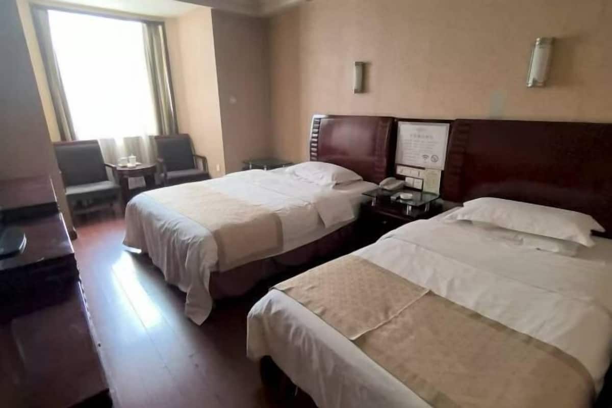 A hotel room with two beds, a small table, a chair, and a window.