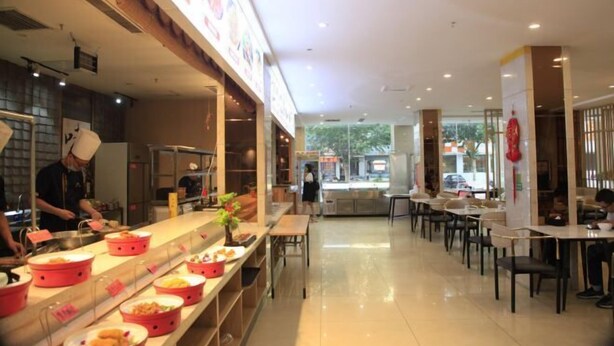 A restaurant with a long counter, multiple tables, and a kitchen area with staff preparing food. - Tianxing Hotel (Lingshi)