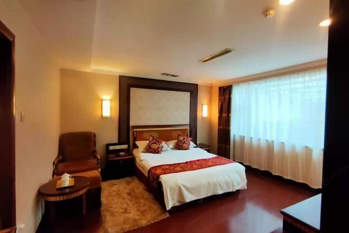 A hotel room with a bed, a chair, a nightstand, a lamp, and a window with curtains.