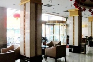 Un vestíbulo de hotel con zonas de estar, un mostrador de recepción y grandes ventanales.