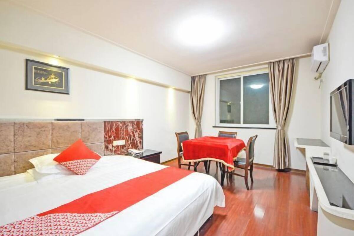 A hotel room with a bed, a desk, a chair, a TV, and a window with curtains.
