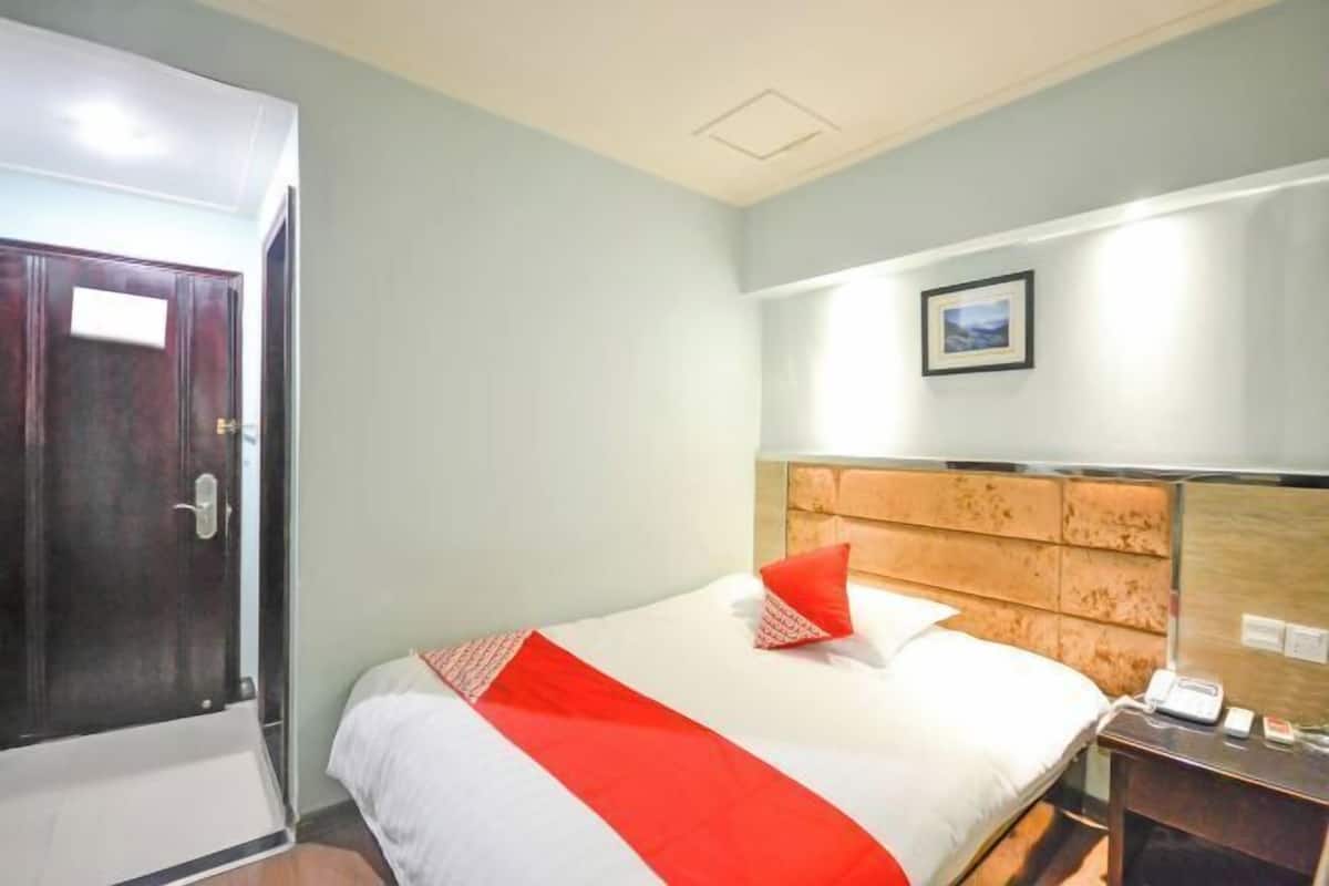 A hotel room with a bed, a wooden headboard, a nightstand, and a door.