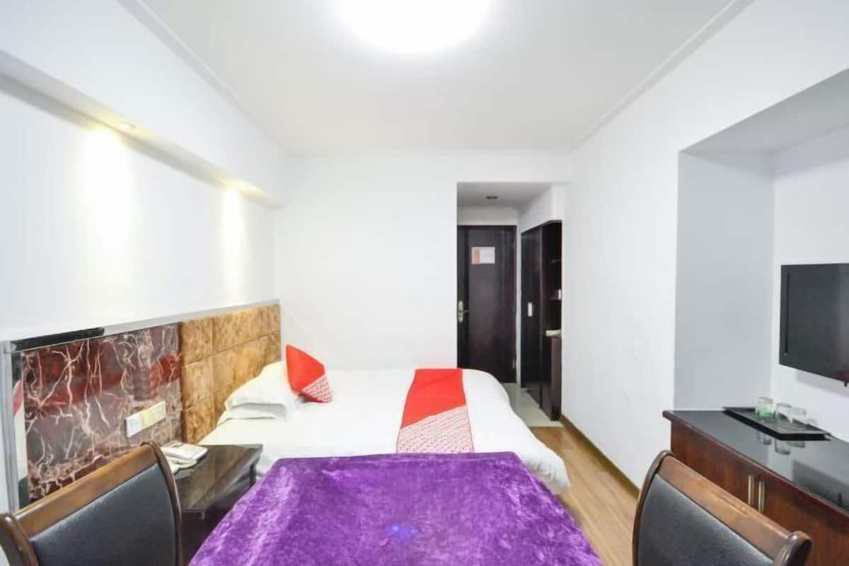 A hotel room with a bed, a desk, a chair, a TV, and a door leading to another room.