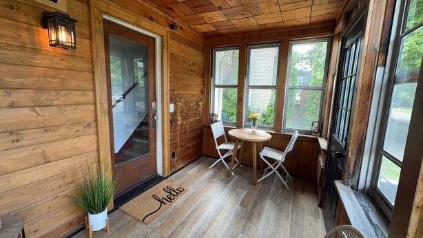 A wooden cabin with a wooden door, a small table with two chairs, and a window with a view of greenery. - Modern Beach Retreat–Pet Friendly + Prime Location (Grand Haven)