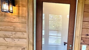 A wooden door with a frosted glass panel, a doormat with "hello" written on it, and a small potted plant beside the door. - Modern Beach Retreat–Pet Friendly + Prime Location (Grand Haven)