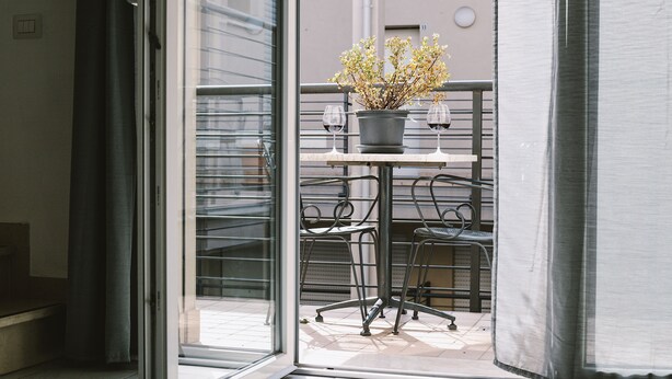 An open sliding glass door leading to a balcony with a potted plant, two wine glasses, and metal chairs. - Firenze Dream Homes - Mona Lisa (Firenze)