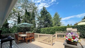 Eine Holzterrasse mit Grill, Gartenmöbeln und Blumenarrangements.