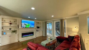 Ein Wohnzimmer mit Flachbildfernseher, Kamin, roten Sofas und Blick durch große Fenster.
