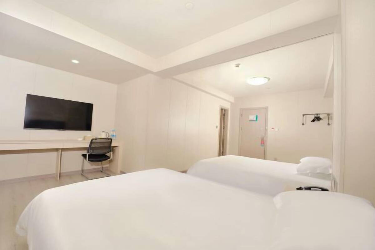 A hotel room with two beds, a desk, a chair, a flat-screen TV, and a door leading to a bathroom.
