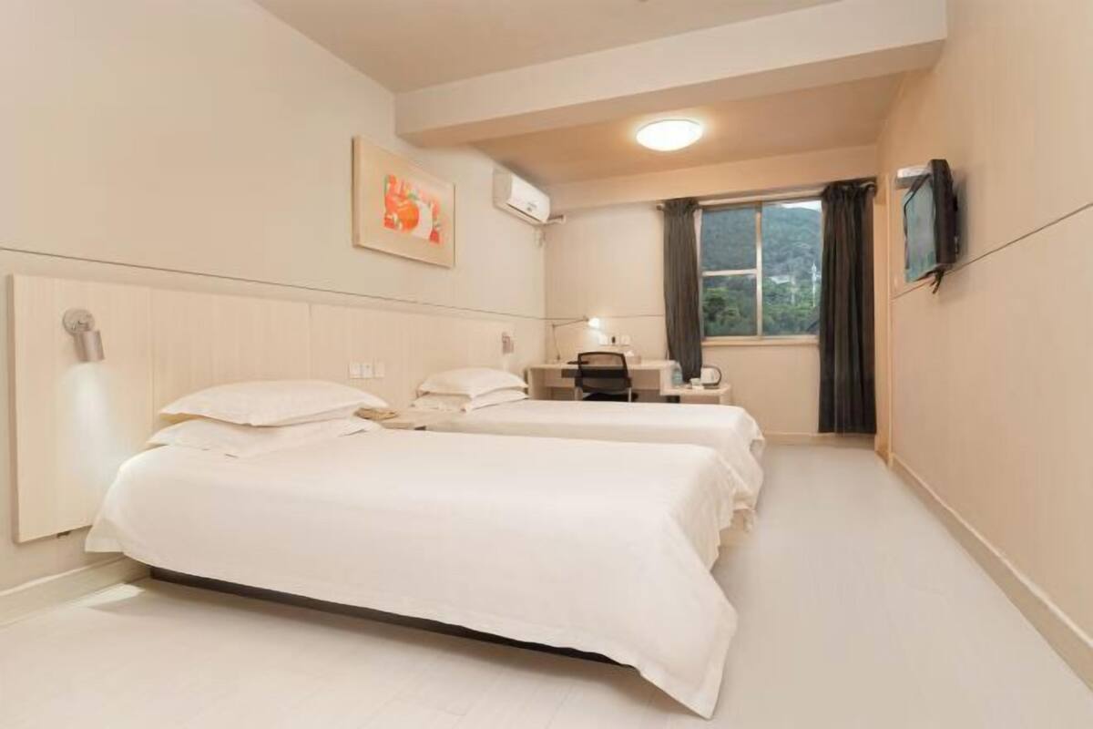 A hotel room with two beds, a desk, a chair, a TV, and a window with curtains.