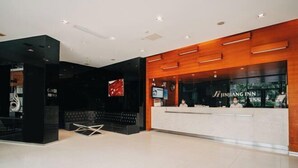 Een moderne hotellobby met een receptiebalie, een zithoek en een groot scherm.