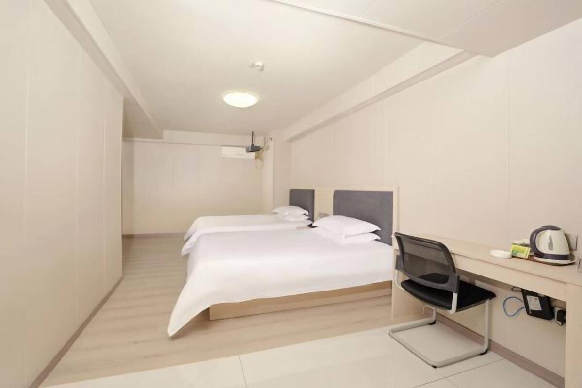 A hotel room with a bed, a desk with a chair, and a kettle.