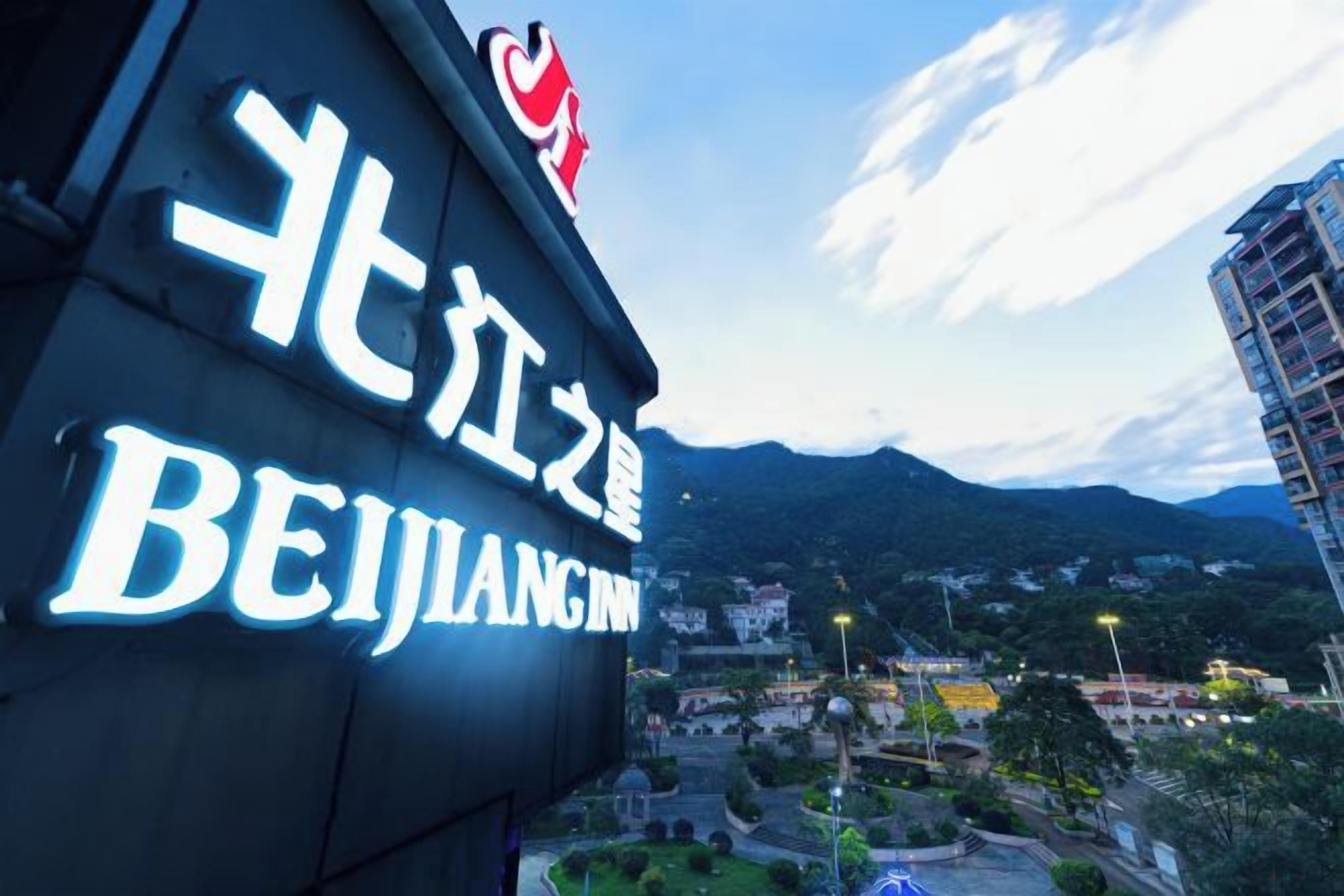 Ein Hotelschild mit fremdsprachiger Schrift und Blick auf eine Stadtlandschaft mit Bergen im Hintergrund.
