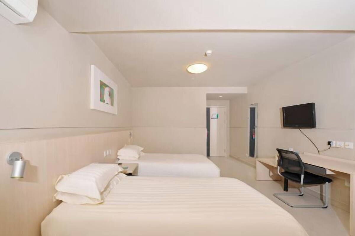 A hotel room with two beds, a desk, a chair, a TV, and a picture on the wall.