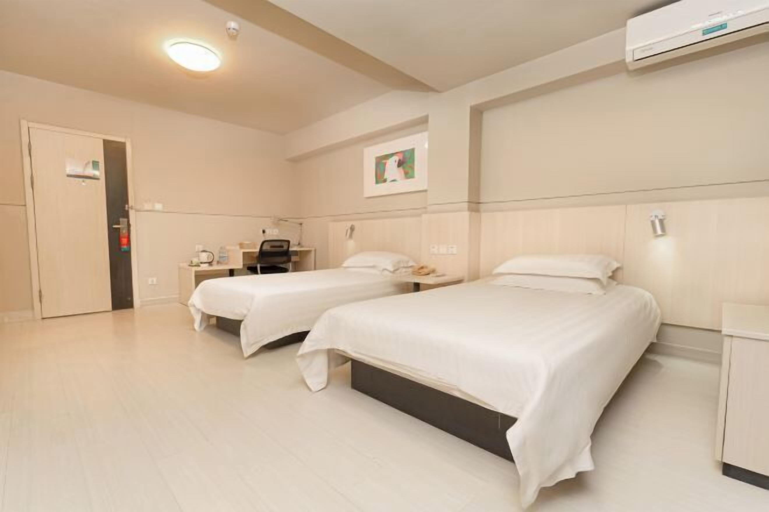 Une chambre d’hôtel avec deux lits, un bureau, une chaise, une armoire et un appareil de climatisation.