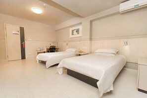 A hotel room with two beds, a desk, a chair, a wardrobe, and an air conditioning unit.