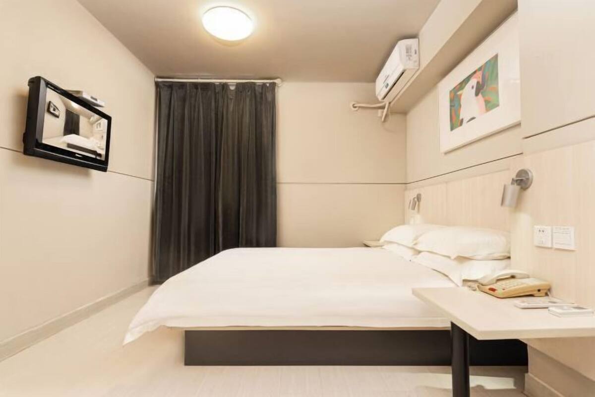 A hotel room with a bed, bedside table, and a wall-mounted TV.