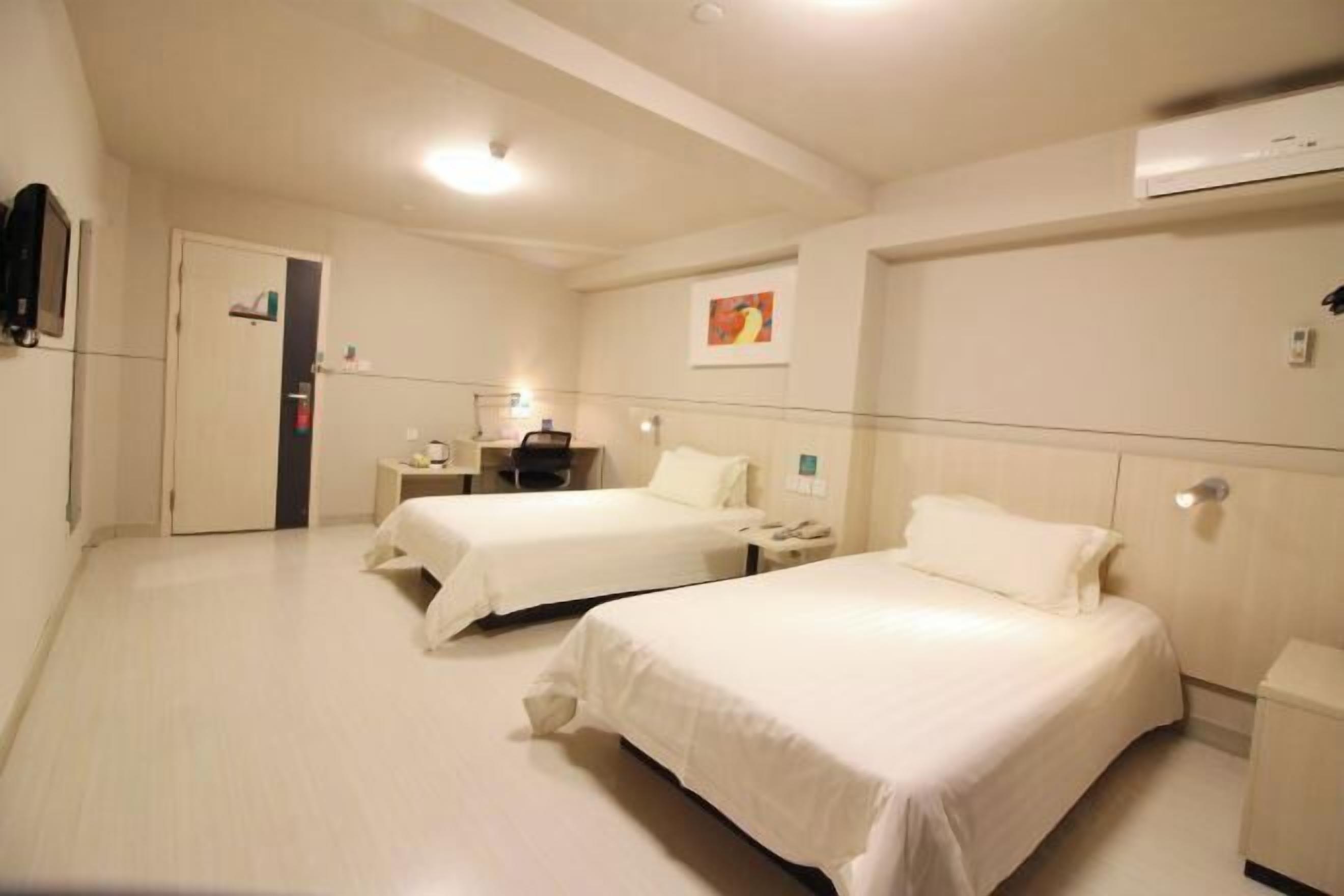 Une chambre d’hôtel avec deux lits, une table de chevet avec une lampe, un petit bureau et un climatiseur fixé au mur.
