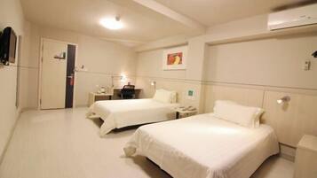 Une chambre d’hôtel avec deux lits, une table de chevet avec une lampe, un petit bureau et un climatiseur fixé au mur.
