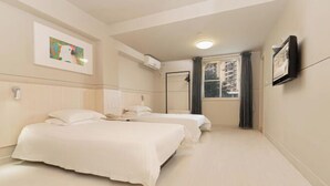 Een hotelkamer met twee bedden, een raam met gordijnen, een aan de muur bevestigde flatscreen televisie en een plafondlamp.