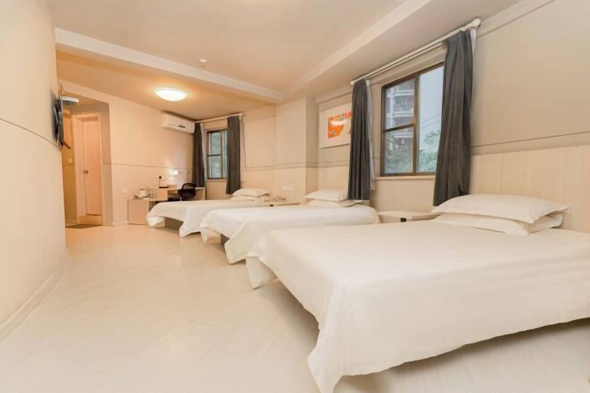 A hotel room with three single beds, a small kitchenette, and a bathroom.