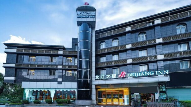 Een meerlaags hotel met een opvallende toren, een bord met de tekst Beijing Inn, en een goed onderhouden buitenruimte met beplanting.