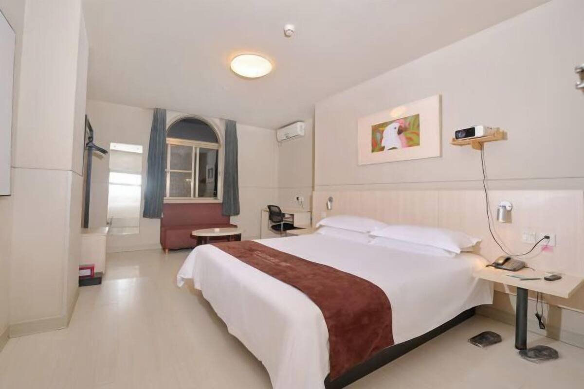 A hotel room with a bed, a desk, a chair, a mirror, and a window with curtains.