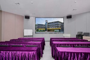 A conference room with rows of tables covered in purple tablecloths, a large screen displaying a building, and a whiteboard. - Beijiang Inn (Qingyuan)