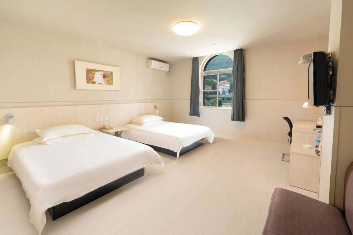 A hotel room with two beds, a window with curtains, a wall-mounted TV, and a small cabinet.