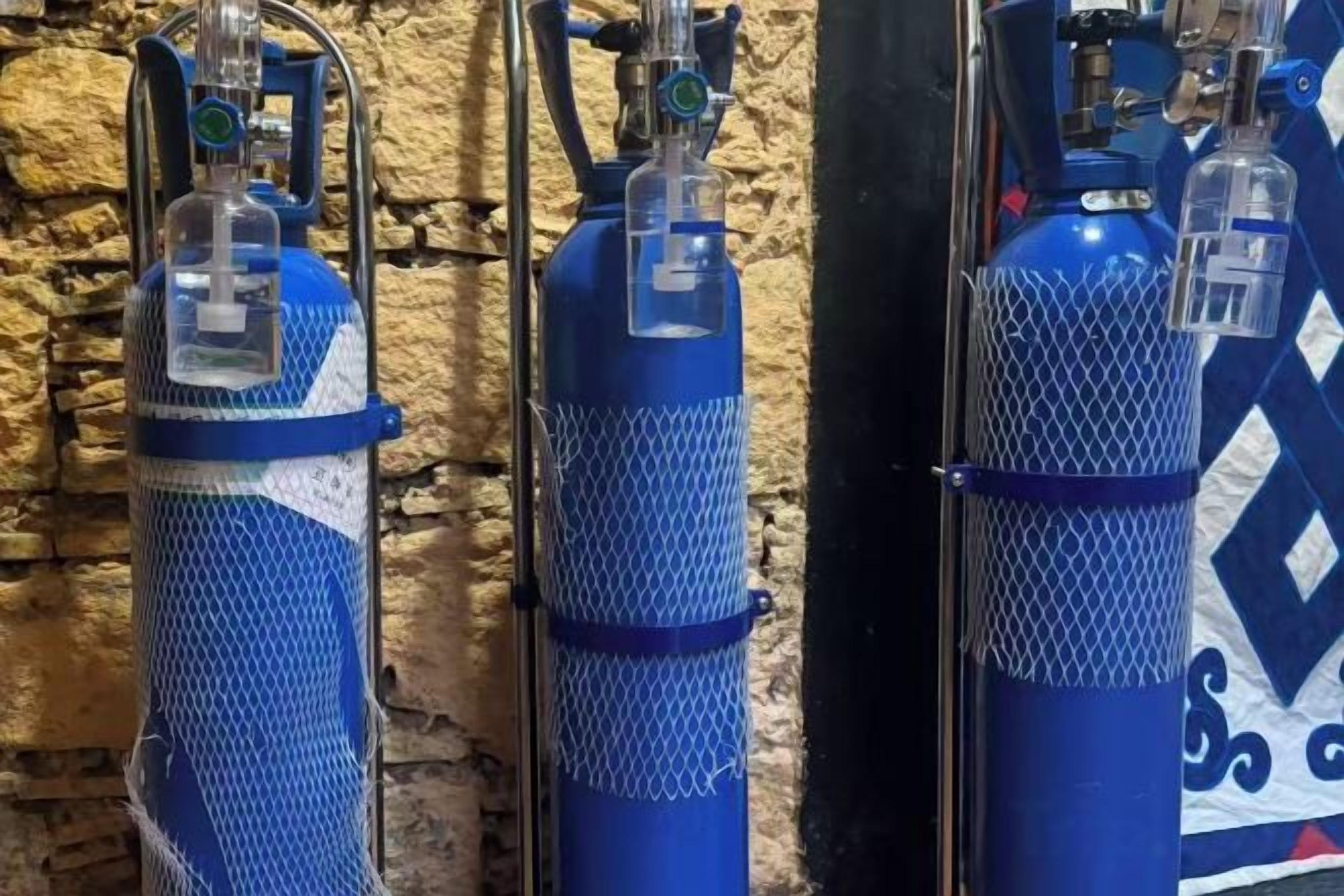 Three blue oxygen tanks against a textured wall.