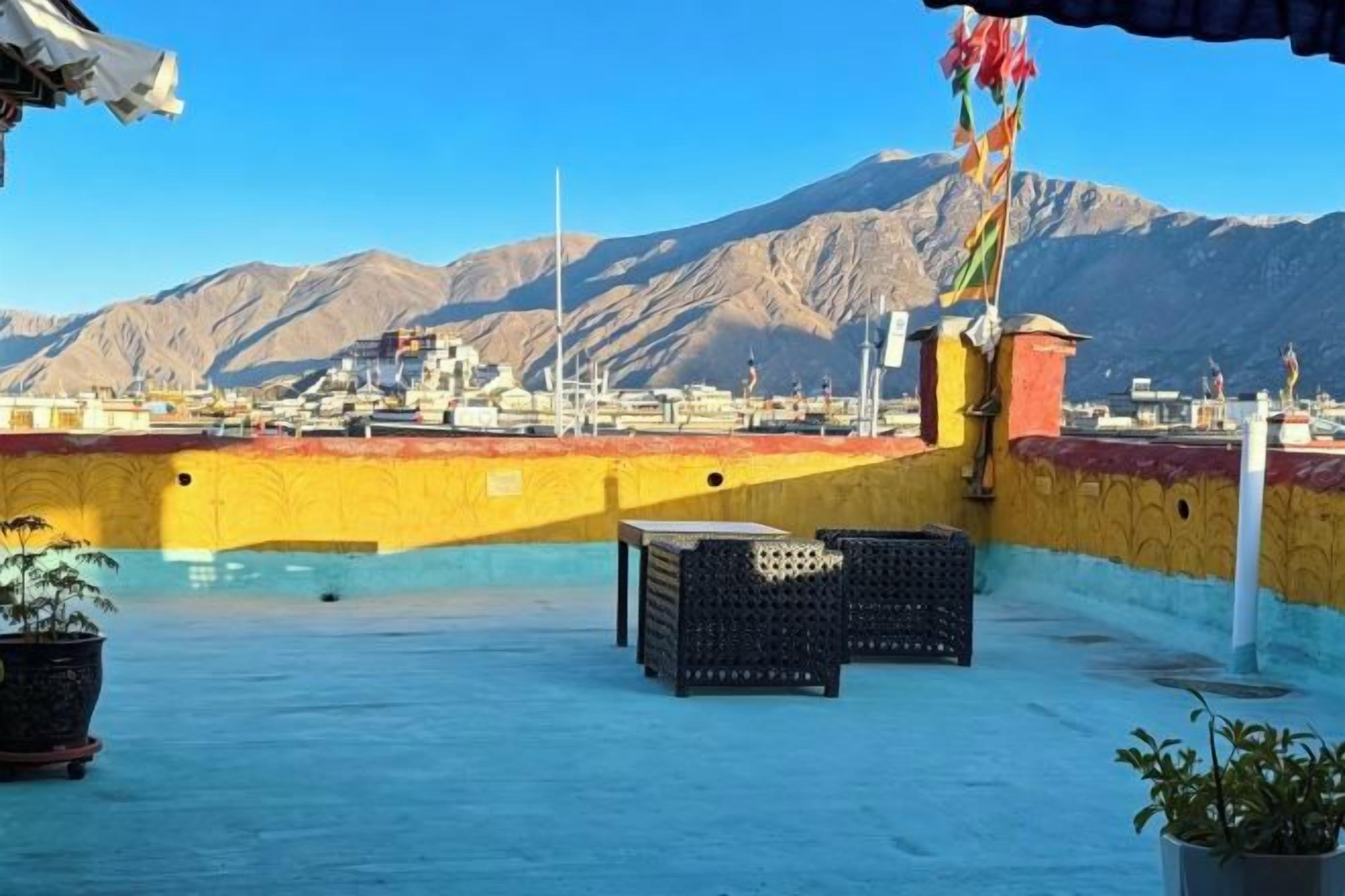 A rooftop terrace with a view of mountains, a flag, and some potted plants.