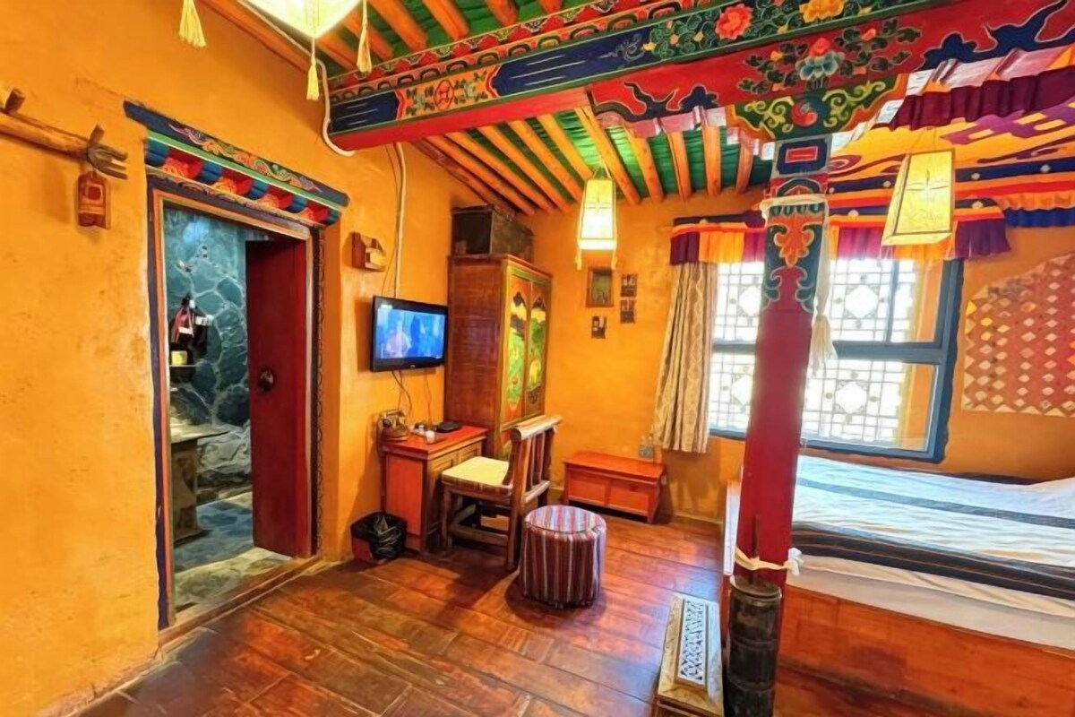 A traditional room with a wooden floor, a television, a bed, and a window with curtains.