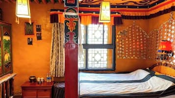 A traditional room with a bed, a wooden desk, and a window with patterned curtains.