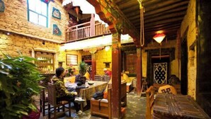 A traditional stone building with a wooden balcony, stone flooring, and a dining area with tables and chairs. - Shambhala Palace Hotel (Lhasa)