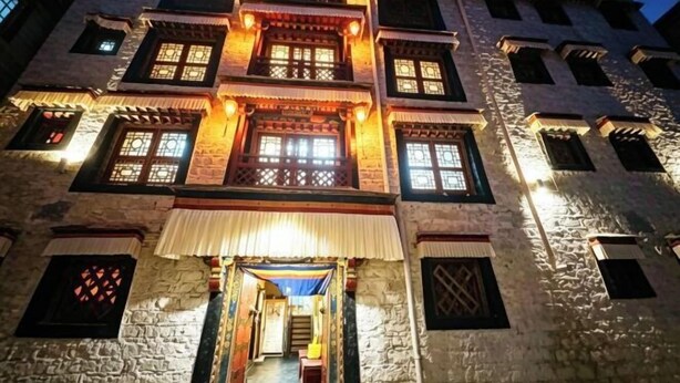 A multi-story building with traditional architecture, featuring a central entrance with a staircase, multiple windows with wooden shutters, and stone walls. - Shambhala Palace Hotel (Lhasa)