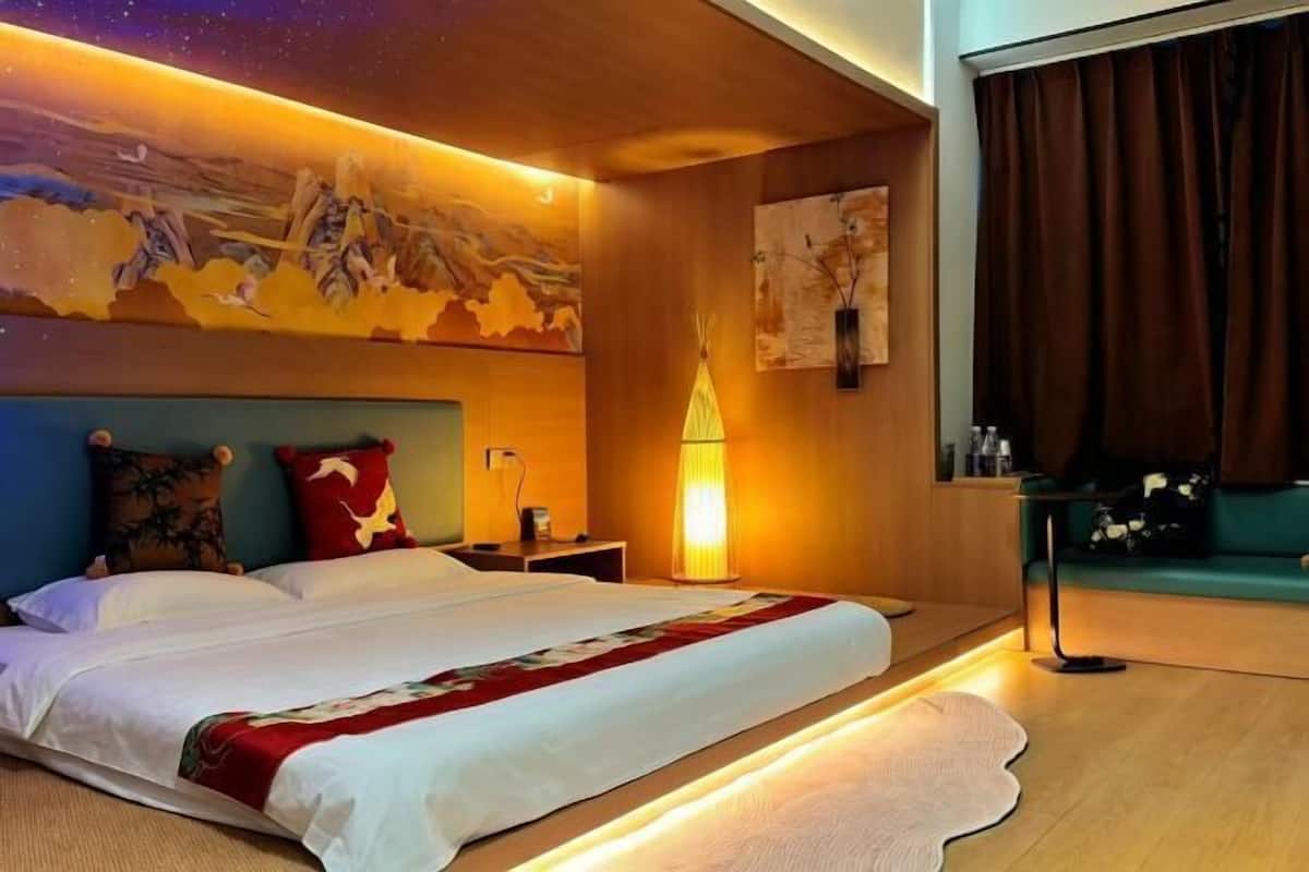 A hotel room with a large bed, a nightstand, a wall-mounted lamp, and a painting.